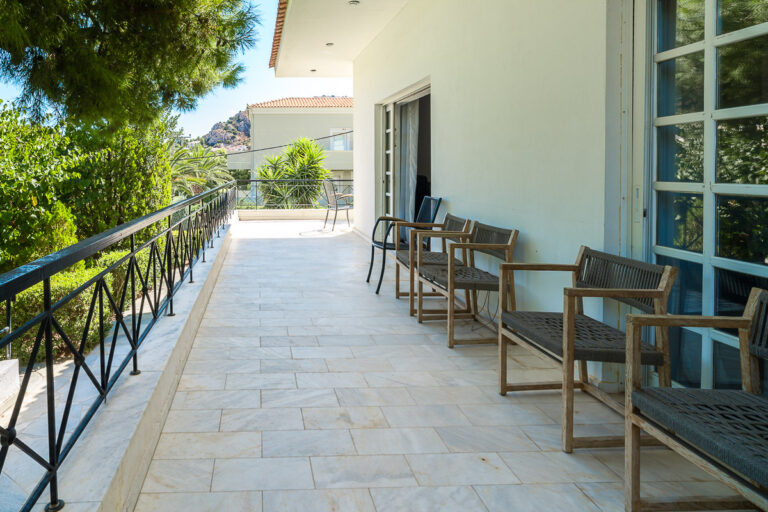 Φωτεινή βεράντα με ανοιχτόχρωμο πλακόστρωτο, ξύλινες καρέκλες και μαύρο μεταλλικό κιγκλίδωμα, φωτογράφιση ακινήτου