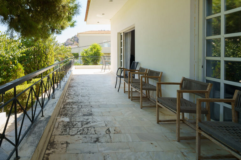 Πλακόστρωτη βεράντα με ξύλινες καρέκλες, μεταλλικό κιγκλίδωμα και πλούσια βλάστηση, φωτογράφιση ακινήτου